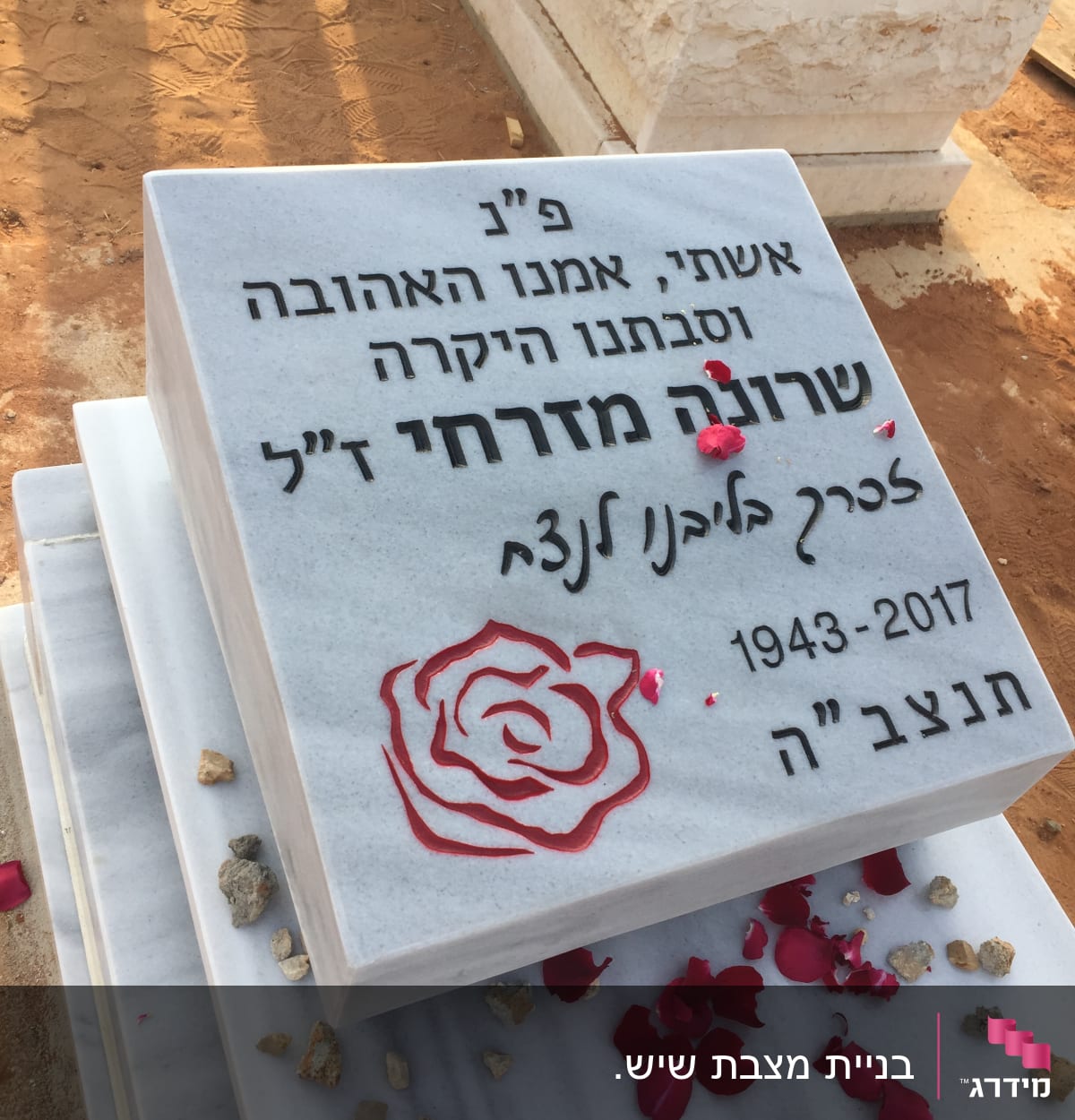 מצבה עם כיתוב בעברית ופרחים אדומים